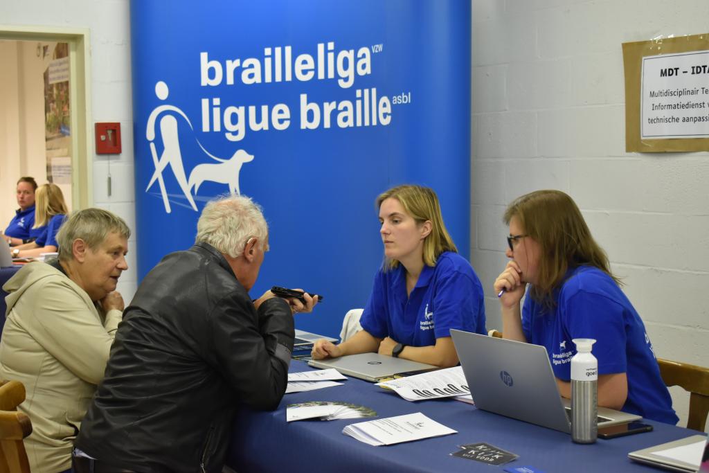 Photo montrant deux thérapeutes de la Ligue Braille répondant aux questions d'un homme sur les smartphones, lors du salon BrailleTech.